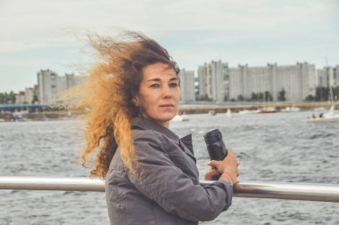 Elinde termosla setin üzerinde duran kız denize bakıyor.