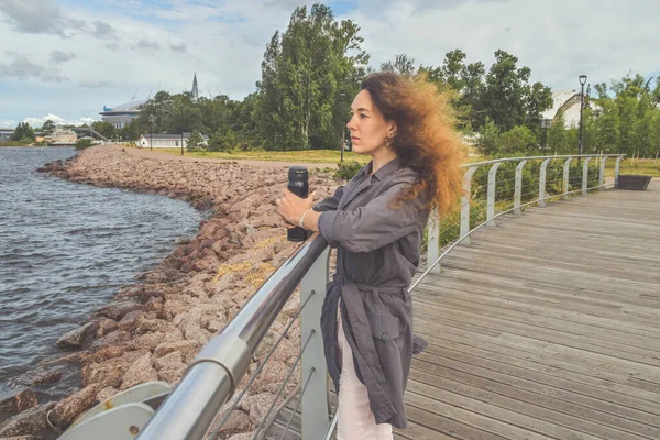 Elinde termosla setin üzerinde duran kız denize bakıyor.