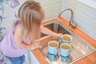 Bir çocuk lavabodaki fincanları filtresiz yıkıyor.
