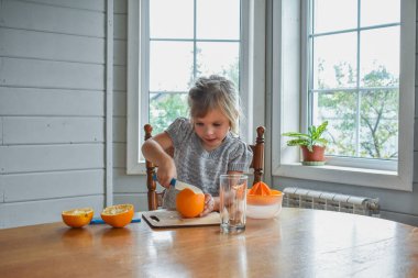 Mutfakta bir kız çocuğu portakal suyunu keser ve sıkar.