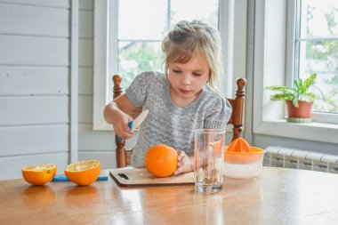 Mutfakta bir kız çocuğu portakal suyunu keser ve sıkar.