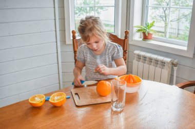 Mutfakta bir kız çocuğu portakal suyunu keser ve sıkar.