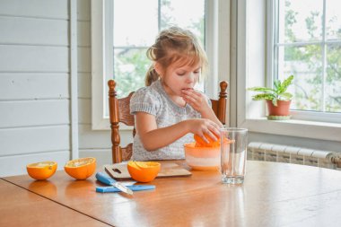 Mutfakta bir kız çocuğu portakal suyunu keser ve sıkar.