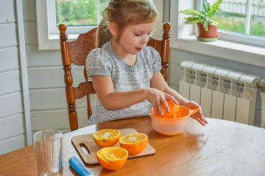 Mutfakta bir kız çocuğu portakal suyunu keser ve sıkar.