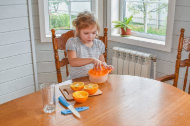 Mutfakta bir kız çocuğu portakal suyunu keser ve sıkar.