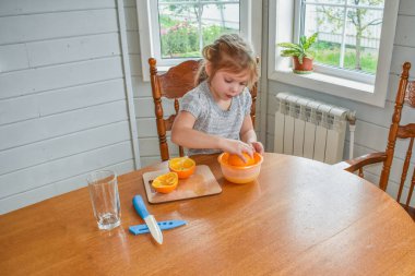 Mutfakta bir kız çocuğu portakal suyunu keser ve sıkar.