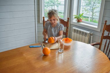 Mutfakta bir kız çocuğu portakal suyunu keser ve sıkar.