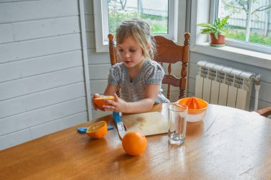 Mutfakta bir kız çocuğu portakal suyunu keser ve sıkar.