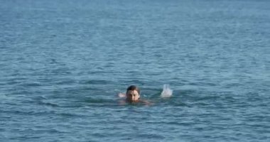 Adam denizde yüzüyor. Günbatımında okyanus dalgalarında yıkanan adam. Aktif açık hava eğlencesi. Yaz titreşimleri. Doğayla birlik.