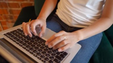 Kadın, kırmızı tuğlalı duvarları olan bir kafede çalışıyor. Laptop klavyesinde kadın tipler. Çatı katı iç mimarisi ile ortak çalışma merkezi. Serbest iş yeri.