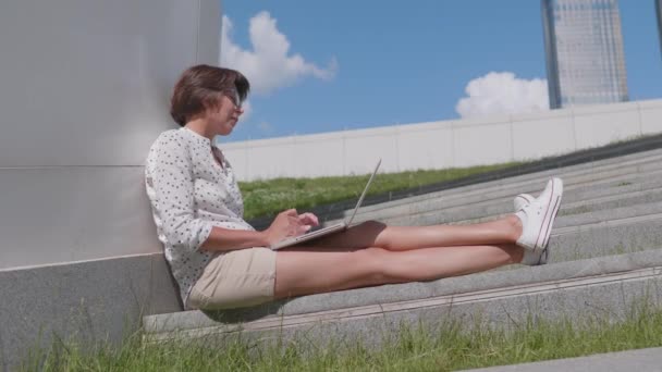 La donna d'affari in occhiali lavora con computer portatile in parco urbano. Posto di lavoro all'aperto per liberi professionisti in estate. — Video Stock