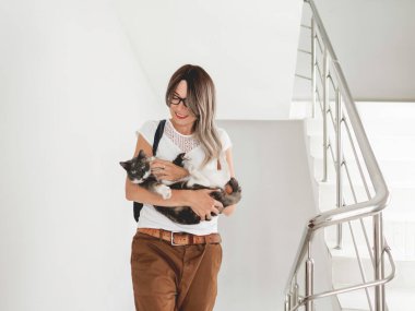 Gülümseyen kadın merdivenlerde sokak kedisini okşar. Gönüllü, evcil olmayan bir hayvanı kurtarıyor. Apartmanda beyaz merdiven. Hayvan evlat edinme.