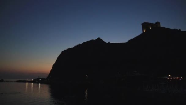 Onderaanzicht op silhouet van het oude Genuese fort in Sudak stad. Panoramaafter zonsondergang. Krim. — Stockvideo