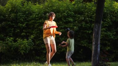 Anne ve oğlu çimlerin üzerinde frizbi oynuyorlar. Yaz titreşimleri. Açık hava eğlence aktivitesi. Aile hayatı. Arka bahçede spor maçı.