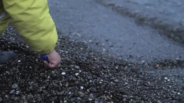 Малюк кидає камінці лопатою для іграшок. Відпочинок на морі для дітей. Активні ігри з натуральними матеріалами на відкритому повітрі . — стокове відео