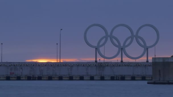 SOCHI, RUSSLAND - 10. März 2020. Olympische Ringe auf dem Hintergrund des Sonnenuntergangs. Symbol der Olympischen Spiele auf dem Wellenbrecher des Hafens von Sotschi. — Stockvideo