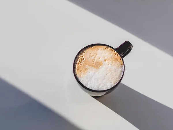 カプチーノのカップの上からの眺め コーヒーマグカップで幾何学的なミニマルな背景 白いテーブルの上に泡のミルクと光 影と熱い飲み物 — ストック写真