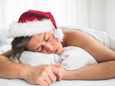 Kırmızı Noel Baba şapkalı adam Noel 'den ya da yeni yıl kutlamasından sonra uyuyor. Sabahın erken saatlerinde yatak odasında ışıkla aydınlandı..