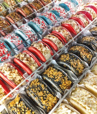 Renkli badem kurabiyeleriyle çapraz bileşim. Sos ve fındıklı lezzetli hamur işlerinin yakın plan fotoğrafı. Krem şantili gökkuşağı renkli kekler..