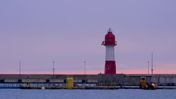 Oude vuurtoren met rode en witte strepen op paarse hemelse achtergrond. Navigatie apparaat in de haven van Sochi bij zonsondergang. Rusland. — Stockvideo