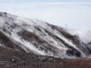 Avacha yanardağı olarak da bilinen Avachinsky stratovolcano 'nun coldera' sında yürüyüş yapan adamın silueti. Sırt çantalı turist sıcak gayzerlerden çıkan buharın arkasındaki kayaların üzerinde hareket ediyor. Kamçatka Yarımadası, Rusya.