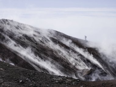 Avacha yanardağı olarak da bilinen Avachinsky stratovolcano 'nun coldera' sında yürüyüş yapan adamın silueti. Sırt çantalı turist sıcak gayzerlerden çıkan buharın arkasındaki kayaların üzerinde hareket ediyor. Kamçatka Yarımadası, Rusya.