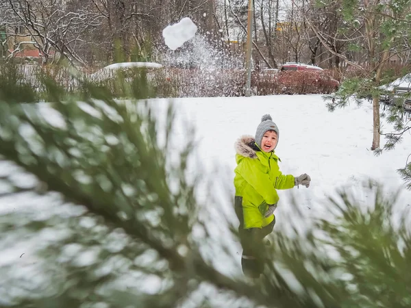 Vreugdevolle Jongen Groene Jumpsuit Speelt Sneeuwbal Besneeuwde Tuin Tussen Pijnbomen — Stockfoto