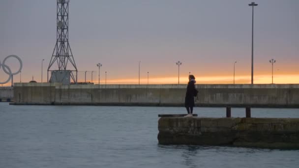 SOCHI, RUSSLAND - 02. März 2020. Silhouette einer Frau auf einer Buhne. Hafen mit Symbol der Olympischen Spiele 2014. — Stockvideo