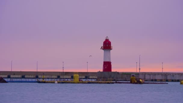 紫の空の背景に赤と白の縞模様の古い灯台。日没時にソチ港のナビゲーション装置。ロシア. — ストック動画