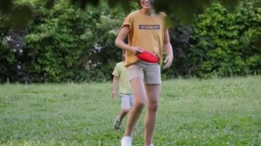 Anne ve oğlu çimlerin üzerinde frizbi oynuyorlar. Yaz titreşimleri. Açık hava eğlence aktivitesi. Aile hayatı. Arka bahçede spor maçı.