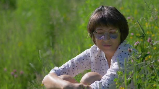Vrouw in kleurrijke zonnebril geniet van zonlicht en bloemengeur op grasveld. Zomer vibes. Ontspan je buiten. Zelfkalmerend. — Stockvideo