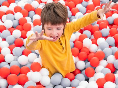 Gülen çocuk top havuzunda oynuyor. Kuru havuzda beyaz ve kırmızı plastik toplar. Anaokulundaki oyun odasında boş zaman aktivitesi. Boş zaman aktivitesi. Etkin yeniden yaratma.