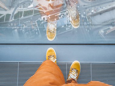Sarı deri ayakkabılı bir adamın ayaklarının üst görüntüsü. Adam binanın üst katındaki panoramik pencerenin yanında duruyor. Bin yılın şehir modası..