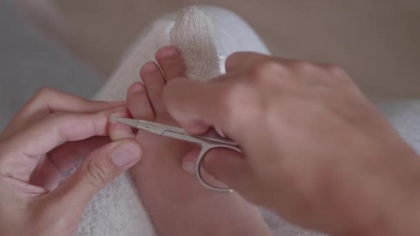 Matka si obvazuje dětský palec a ostříhá nehty o druhou nohu. Detailní záběr dětské nohy s obvázaným prstem. První pomoc v případě malých domácích zranění. — Stock video