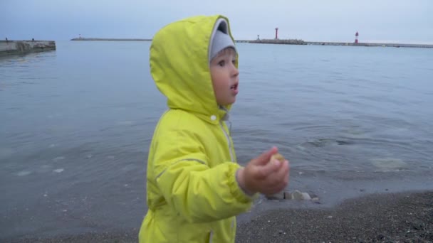 Маленький хлопчик у жовтому костюмі грає на узбережжі Чорного моря. Грайливий хлопчина на пляжі біля морського прибою.. — стокове відео