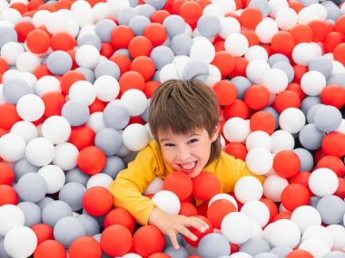 Gülen çocuk top havuzunda oynuyor. Kuru havuzda beyaz ve kırmızı plastik toplar. Anaokulundaki oyun odasında boş zaman aktivitesi. Boş zaman aktivitesi. Etkin yeniden yaratma.