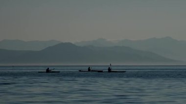 Dağlık arka planda hareket eden kanolardaki turist siluetleri. Rusya 'nın Kamçatka yarımadasında yaz tatili.