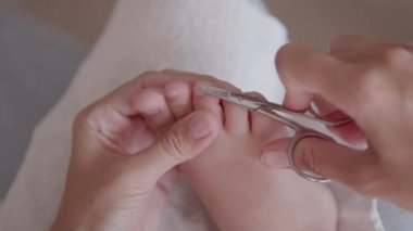 Anne, çocuklarının ayak parmaklarını kesiyor. Çocuk ayağının yakın plan fotoğrafı. Evde cilt bakımı prosedürü.
