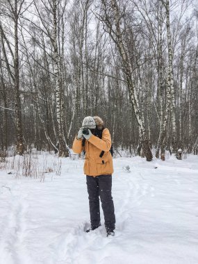 Kış ormanında kameralı bir adam. Fotoğrafçı karların altındaki ağaçların resimlerini çekiyor. Soğuk mevsimde boş zaman aktivitesi.