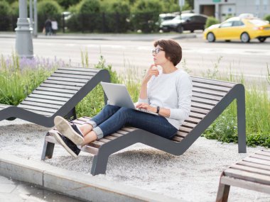 Kadın dizüstü bilgisayarla şehir parkındaki bankta oturuyor. İşyerinde serbest çalışan biri. Öğrenci, dışarıdan uzaktan öğreniyor. Modern yaşam tarzı.