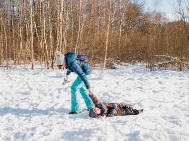Smiling woman carries laughing boy home from winter forest. Family time at nature. Outdoor leisure activity in cold snowy season.