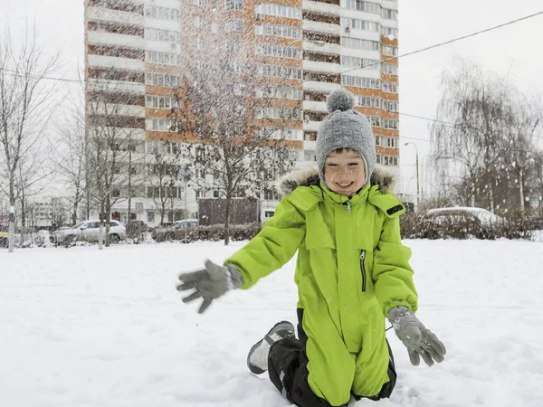 Смеющийся Мальчик Зеленом Комбинезоне Играет Снежок Снежном Дворе Среди Деревьев — стоковое фото