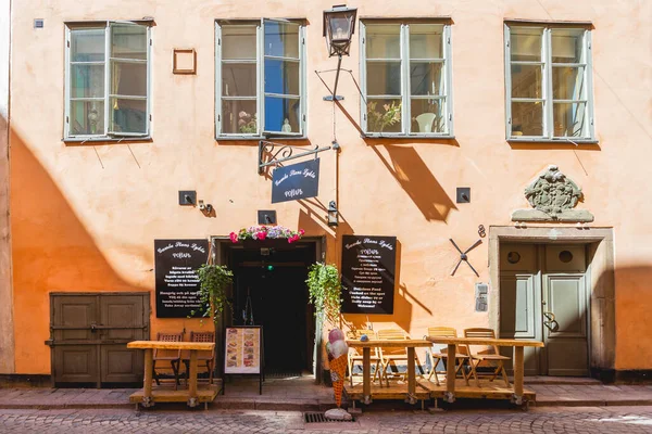 STOCKHOLM, İSVEÇ - 6 Temmuz 2017. Açık kapıları ve açık masaları olan bir kafe. Güneş ışığı Gamla Stan 'in parlak sarı duvarlarına yansıyor. Şehrin tarihi bölgesinde renkli eski moda binalar.
