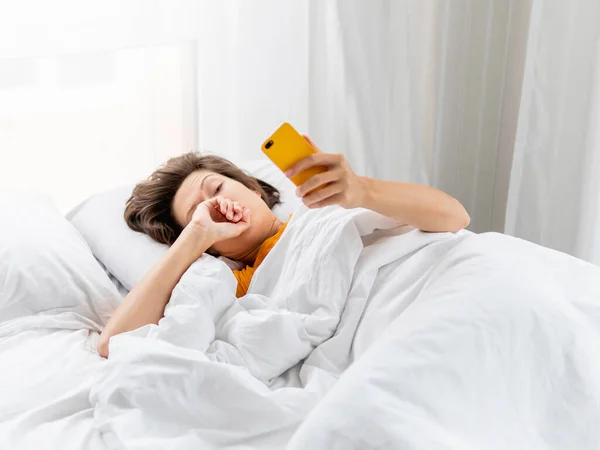 Сонная Женщина Лежит Постели Полностью Покрытая Белым Одеялом Смартфон Используется — стоковое фото