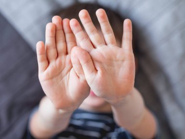 Küçük çocuk elleriyle yüzünü kapatıyor. Çocuğun fotoğrafının çekilmesini reddediyor. Neşeli çocuk gülmek yerine avucunu gösteriyor..