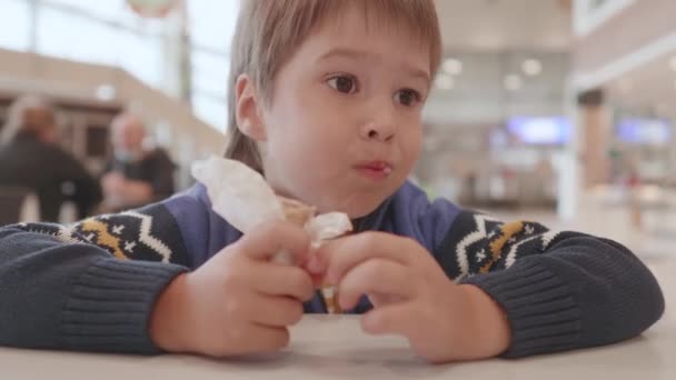Băiețelul mănâncă înghețată în colțul de alimente al mall-ului. Copil mic cu desert rece în cafenea. — Videoclip de stoc