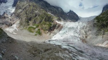 Aerial view of a mountain glacier on a summer day against the backdrop of a cloudy sky.