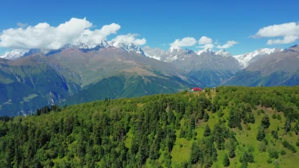 Aerial view of a small house in the forest against the background of snow-capped mountain peaks. — Vídeo de Stock