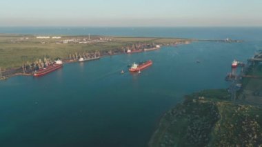 Aerial view of a large cargo ship being driven out of the harbor by tugboats at sunset.