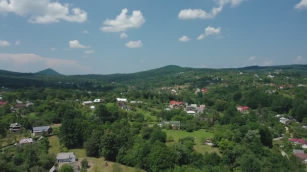 Vue aérienne de maisons de village dans une vallée de montagne contre un ciel bleu avec des nuages occasionnels. — Video